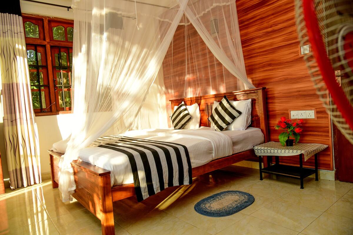 A wooden bed with a canopy, a bedside table with a vase of flowers, and a view of a window with curtains.