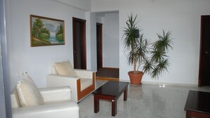 A living room with a white sofa, a coffee table, a potted plant, and a painting on the wall. - Hotel Freskia (Sarandë)