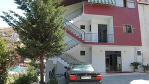 A two-story building with a red and white facade, a staircase leading to the upper floor, and a car parked in front. - Hotel Freskia (Sarandë)
