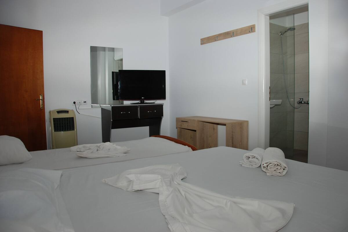 A hotel room with two beds, a TV, a desk, and a shower area.