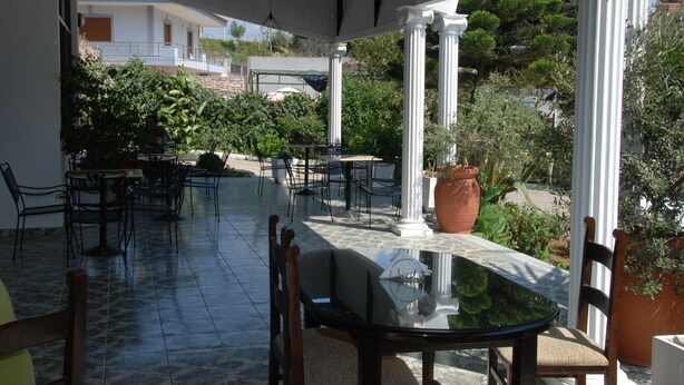 An outdoor patio with a glass table, chairs, and potted plants. - Hotel Freskia (Sarandë)