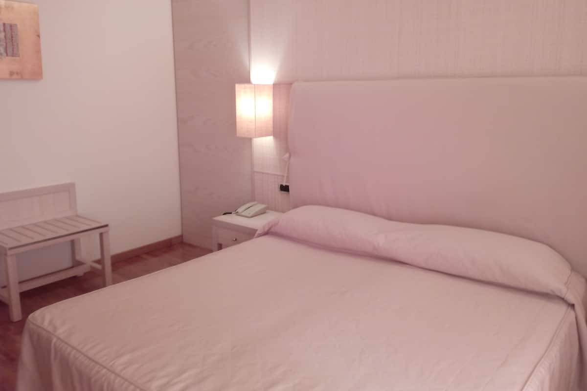 A room with a bed, a bedside table, a lamp, and a wall-mounted phone.