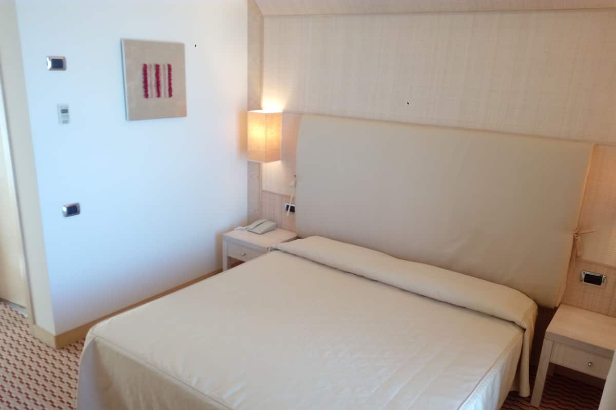 A hotel room with a large bed, bedside tables, a lamp, and a wall-mounted phone.