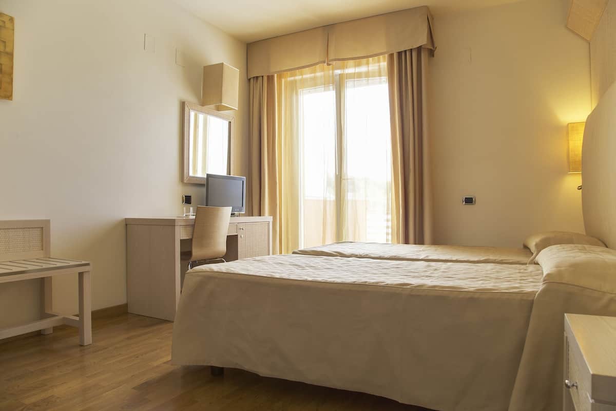 A hotel room with a bed, desk, chair, and a window with curtains.