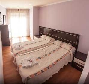 Quarto de hotel com duas camas, piso de madeira, cabeceira e mesa de cabeceira.