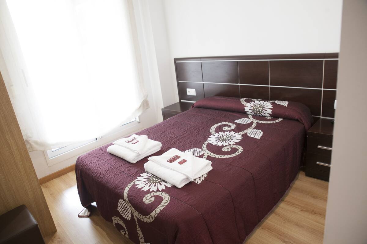 Una cama bien hecha con una colcha estampada y dos toallas dobladas.