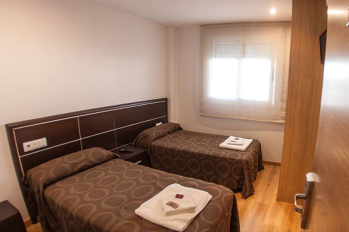 Habitación de hotel con dos camas, piso de madera, una ventana con persianas y una puerta.