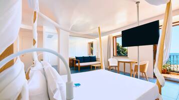 A hotel room with a bed, a desk, a chair, a sofa, a TV, and a balcony with a view of the sea.