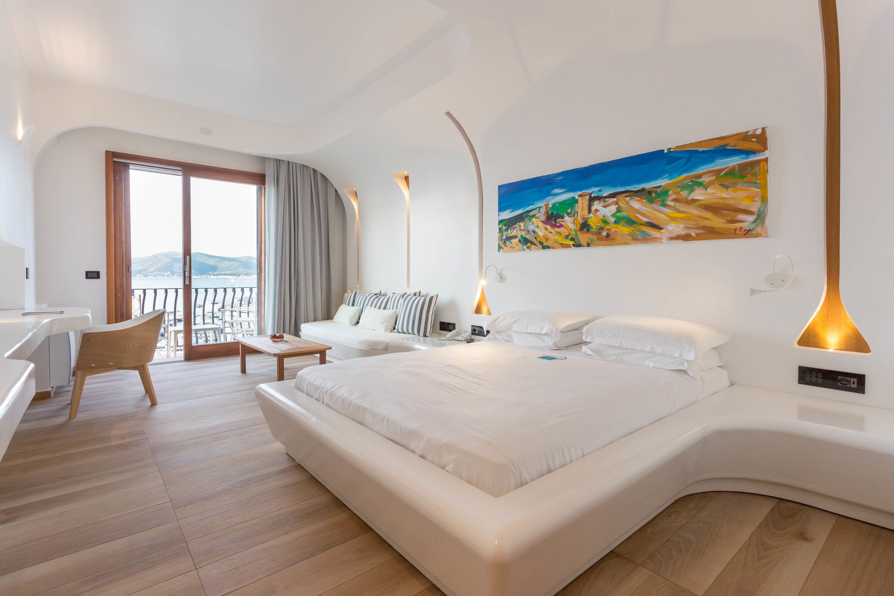 A modern hotel room with a large bed, a desk, a chair, and a balcony with a view.