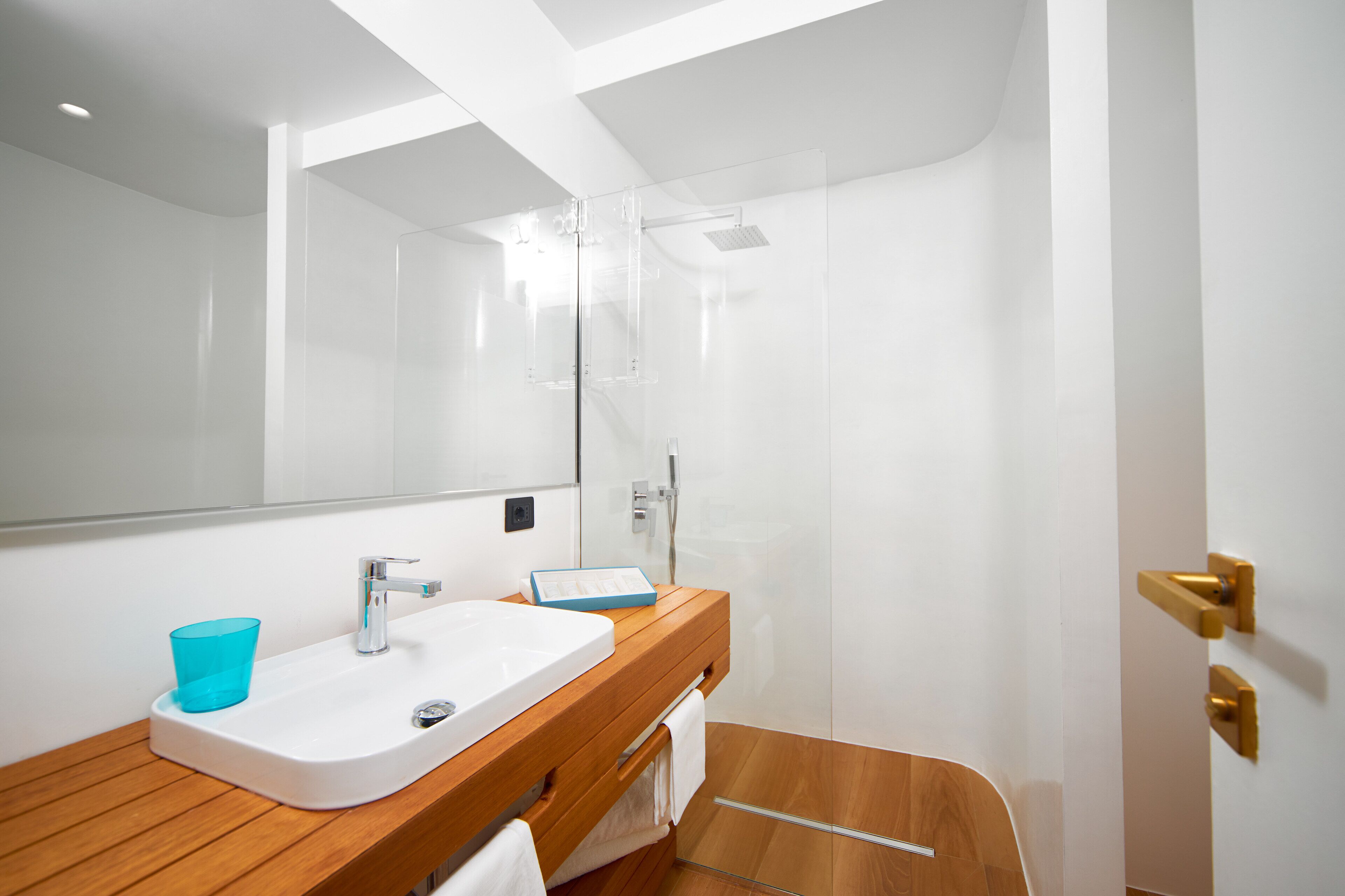 A modern bathroom with a wooden vanity, a white sink, a blue glass, and a glass-enclosed shower.