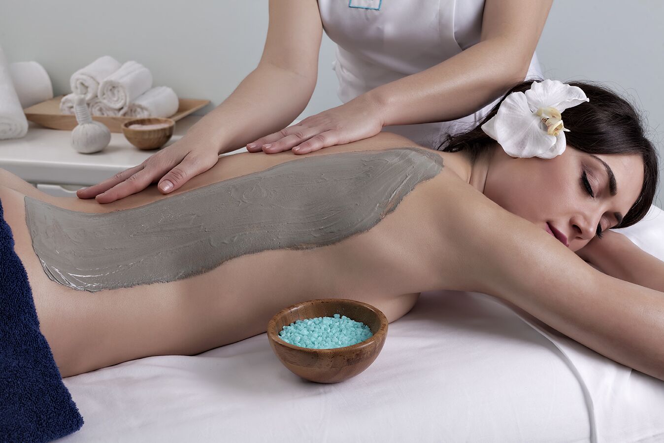 A person receiving a massage with a towel and a bowl of blue crystals on a bed.