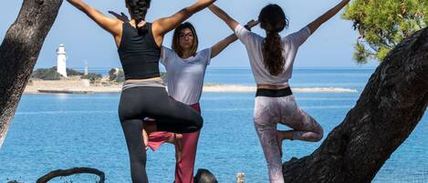 Three people practicing yoga on a mat by the sea, with a lighthouse in the background.