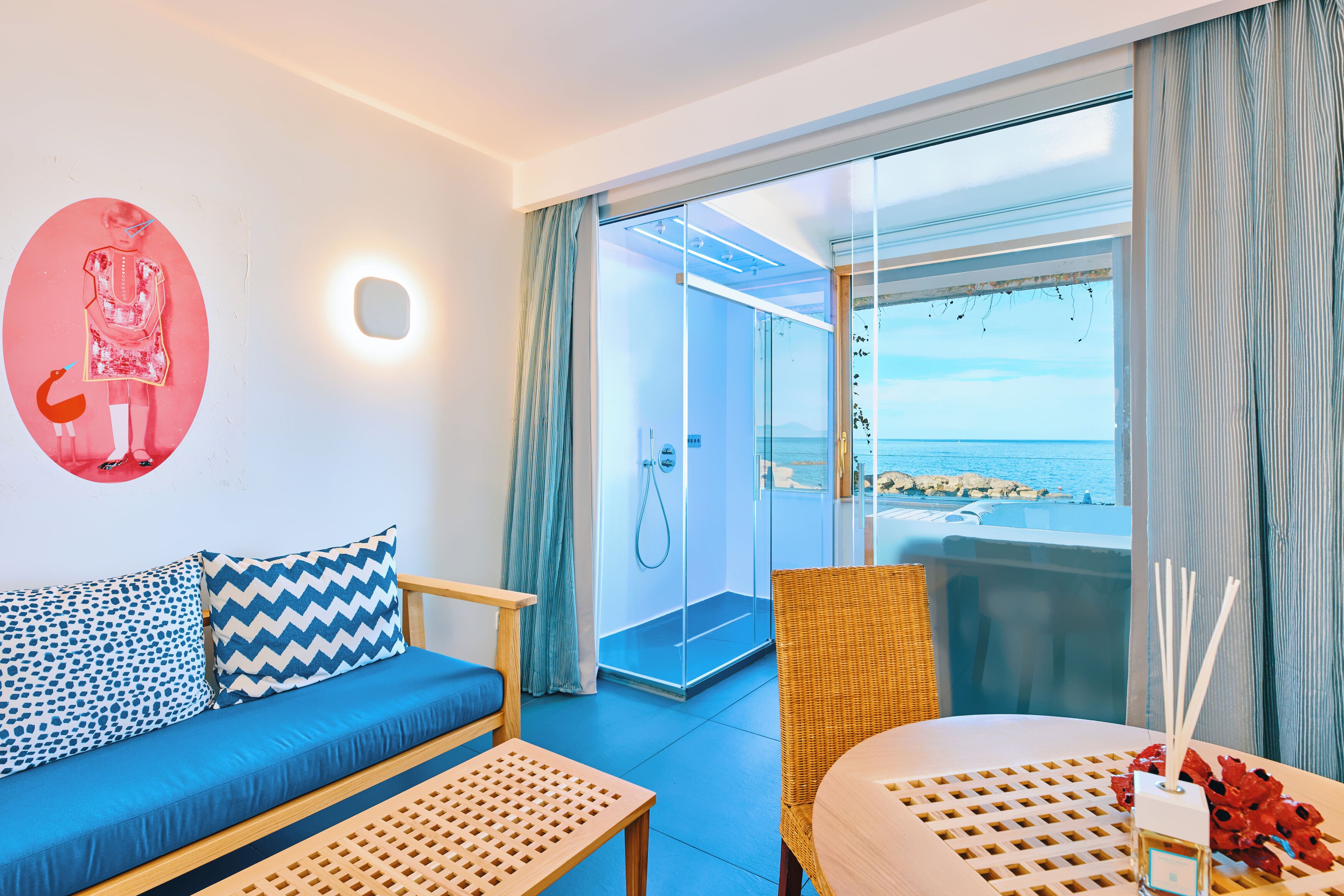 A modern room with a sofa, a table, and a balcony with a view of the sea.