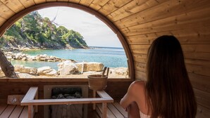 A wooden cabin with a circular window overlooking a beach. Inside, there is a wooden bench and a table with a clock. - Approdo Resort Thalasso Spa (Castellabate)