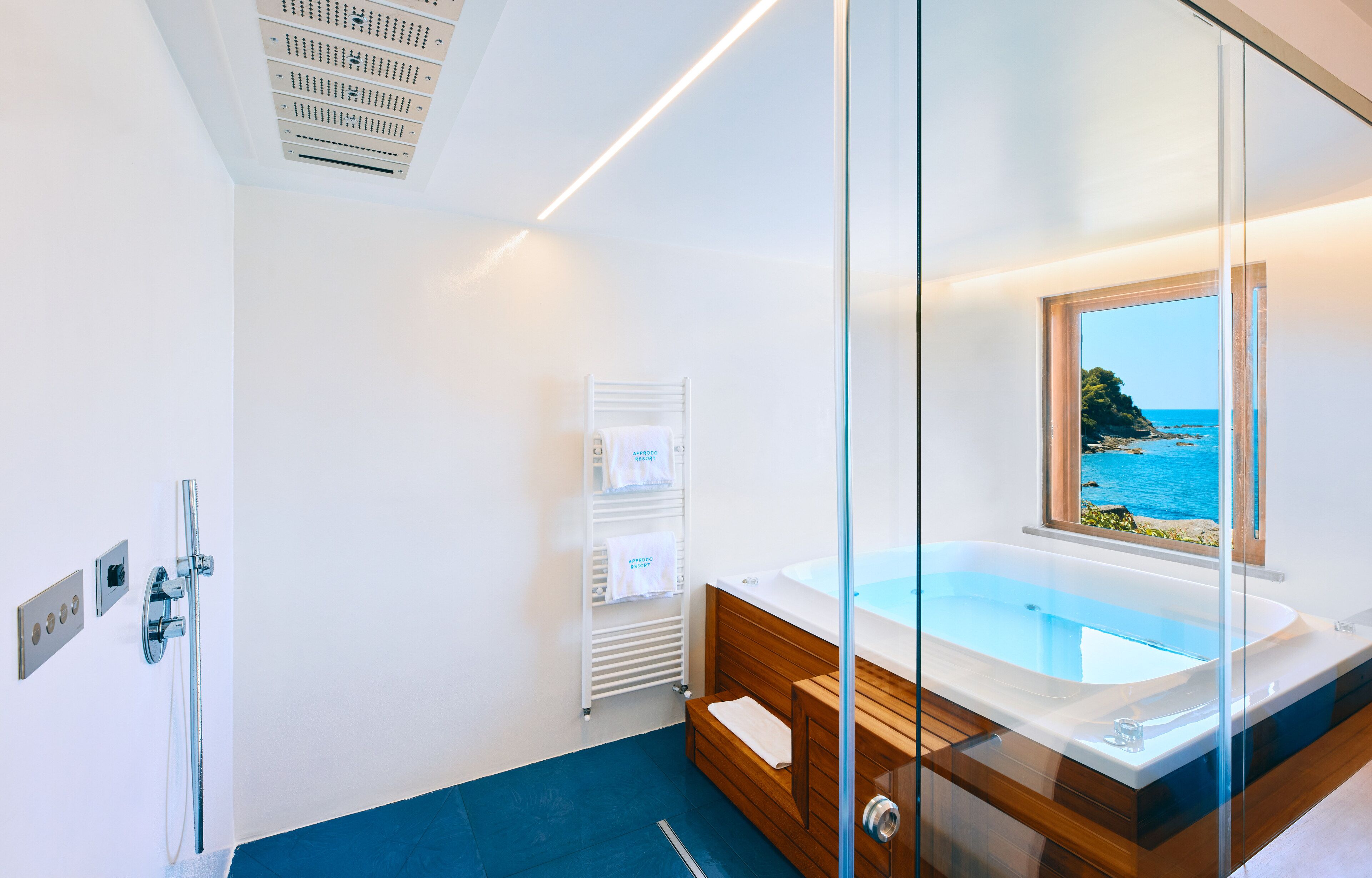 A modern bathroom with a glass-enclosed bathtub, a view of the sea, and a wooden vanity.