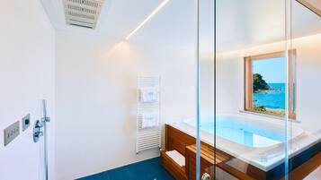 Une salle de bain moderne avec une baignoire entourée de parois en verre, une vue sur la mer et un meuble-lavabo en bois.
