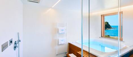 A modern bathroom with a glass-enclosed bathtub, a view of the sea, and a wooden vanity.