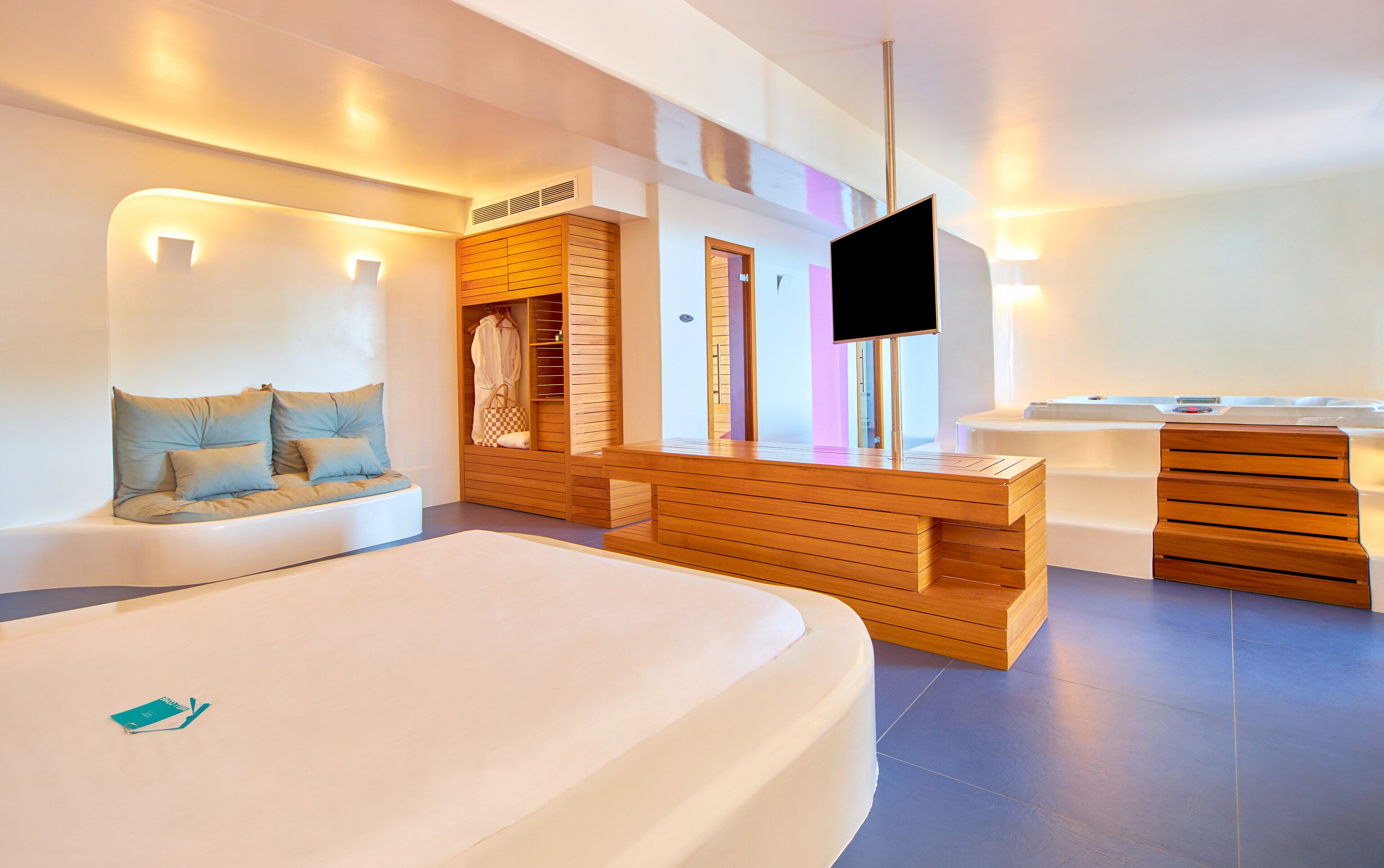 A modern hotel room with a large bed, a wooden bench, a TV, and a bathroom with a bathtub and a shower.