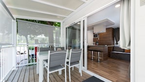 A modern kitchen with a bar area, a dining area with a table and chairs, and a wooden deck with a view of the outdoors. - Luxury Camp at Union Lido (Cavallino-Treporti)