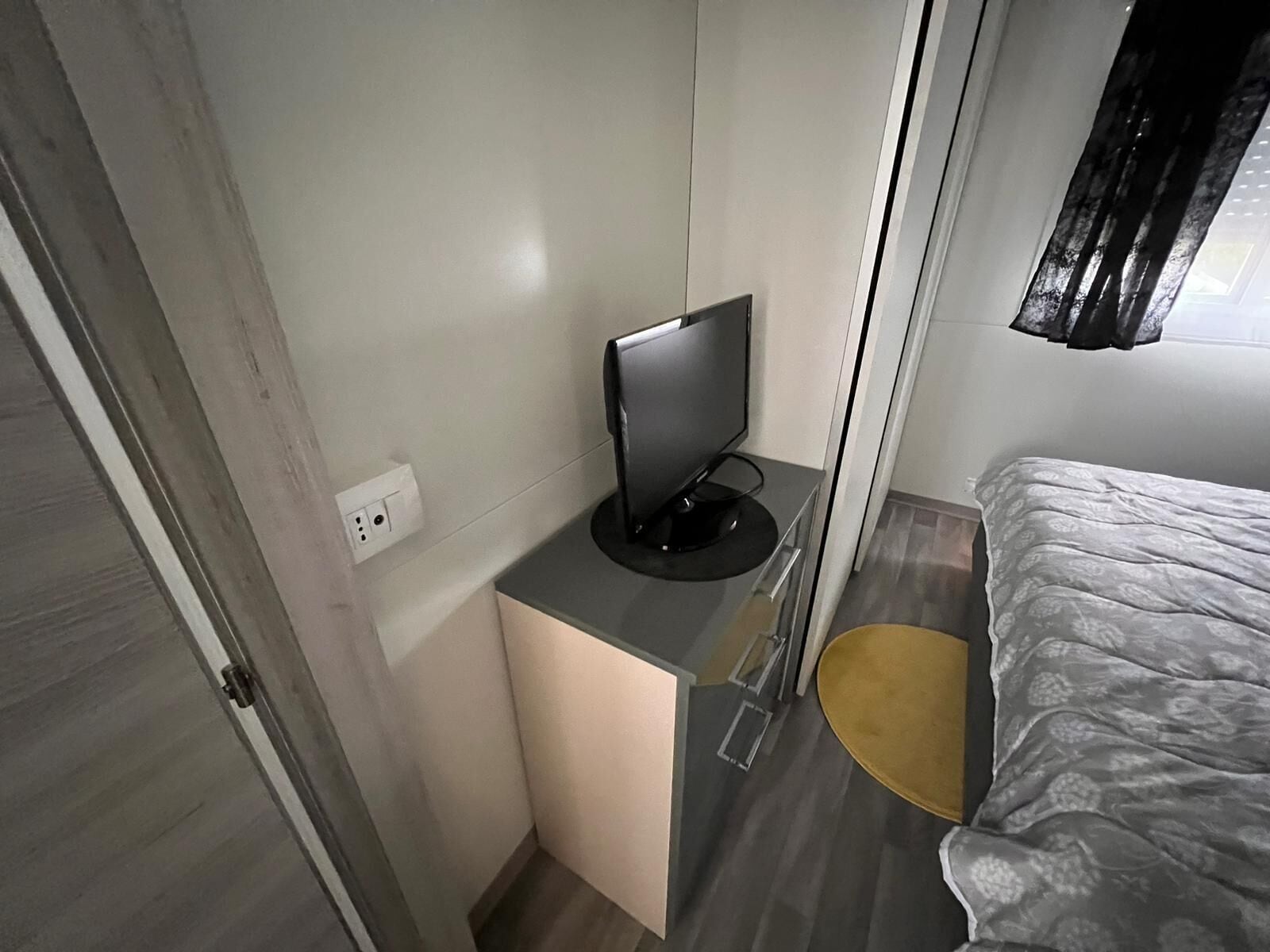 A compact room with a bed, a desk with a computer, and a small chair.