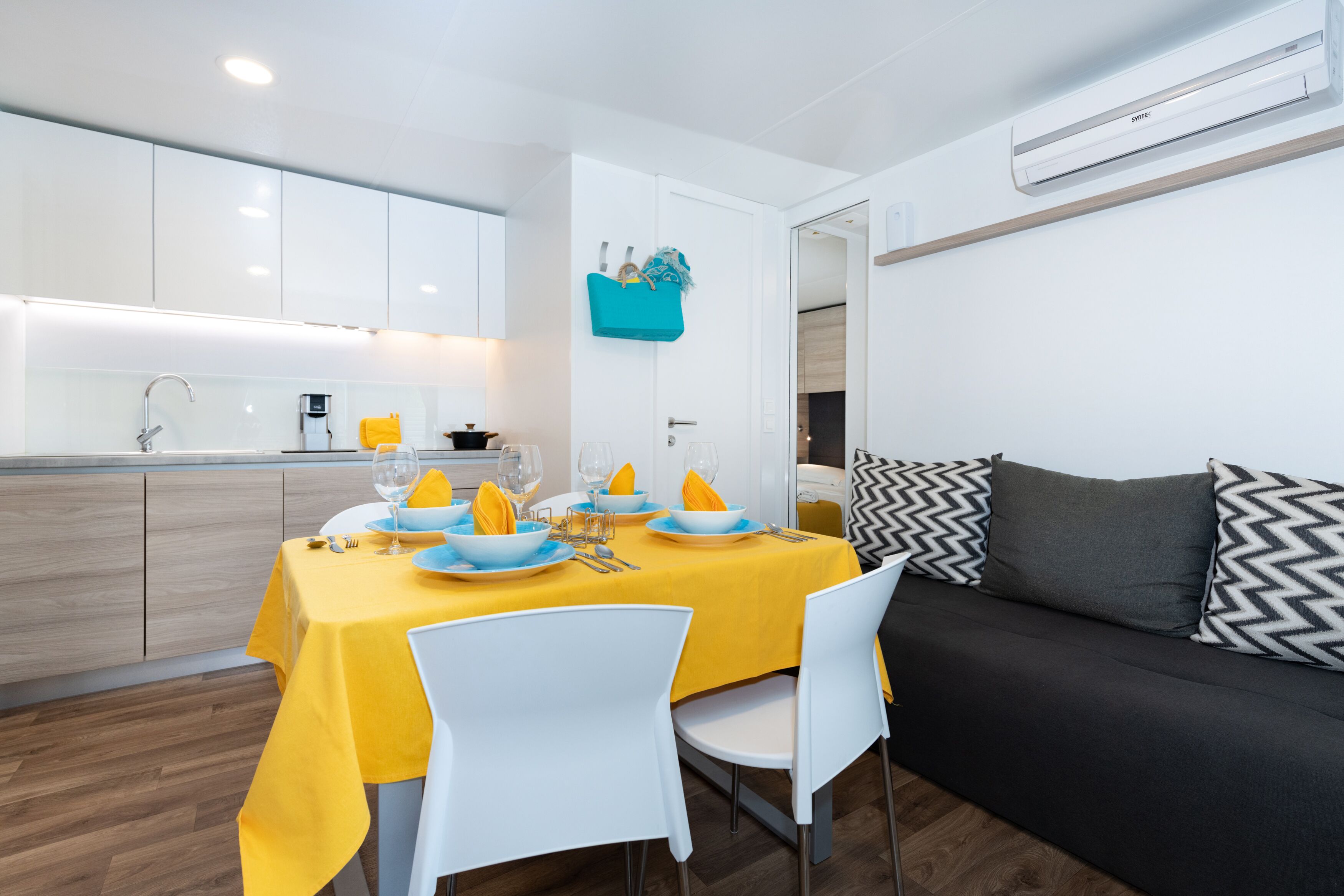 Una cocina moderna con armarios blancos, una mesa de comedor con mantel amarillo y un sofá negro con cojines estampados.