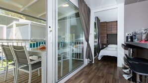 A modern room with a glass door leading to a balcony, a bed with a white mattress, a small kitchen area with a sink and countertop, and a seating area with a table and chairs. - Luxury Camp at Union Lido (Cavallino-Treporti)