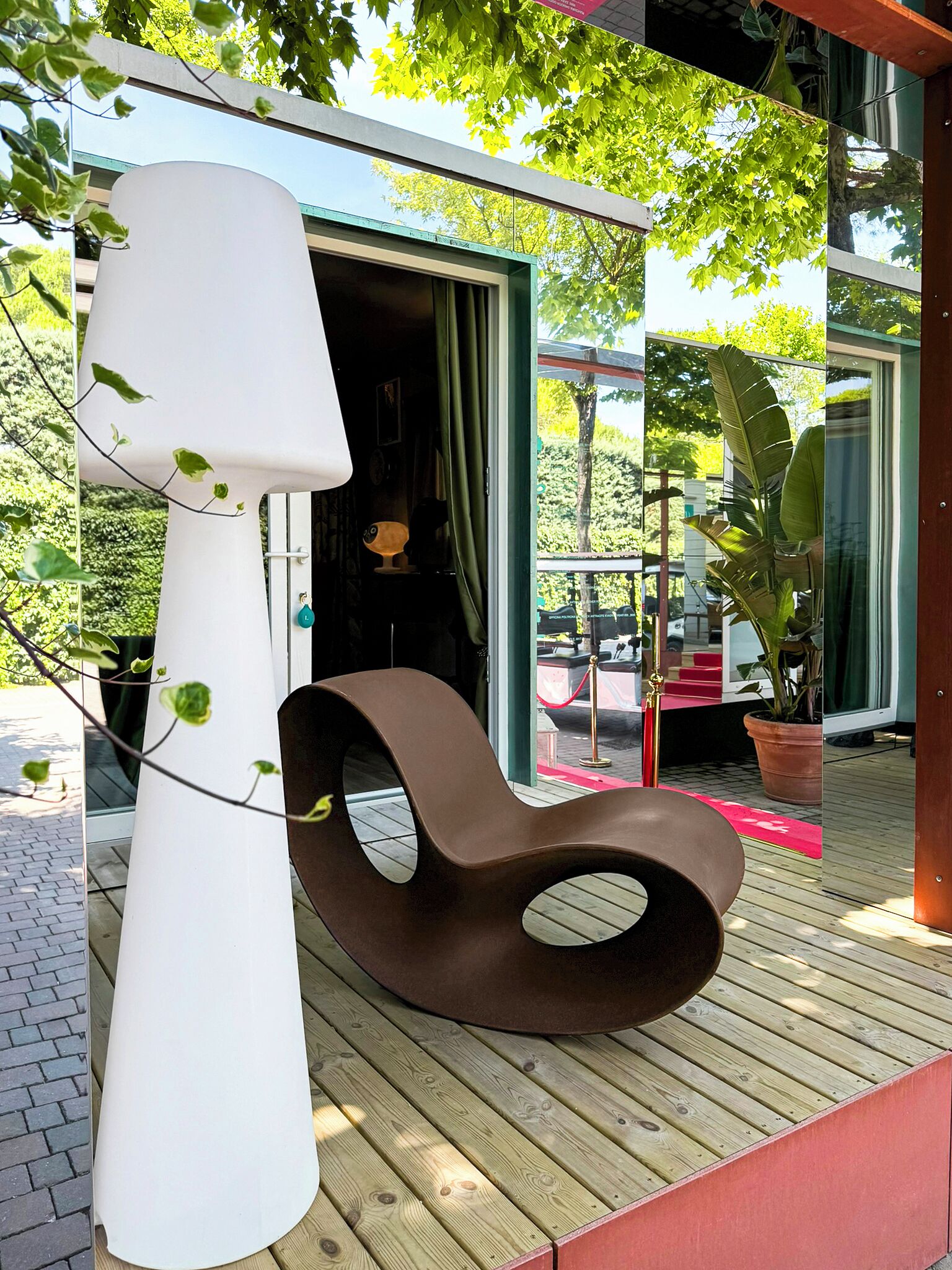 A modern outdoor seating area with a unique chair design, a white pillar, and a view of a building with a glass door.