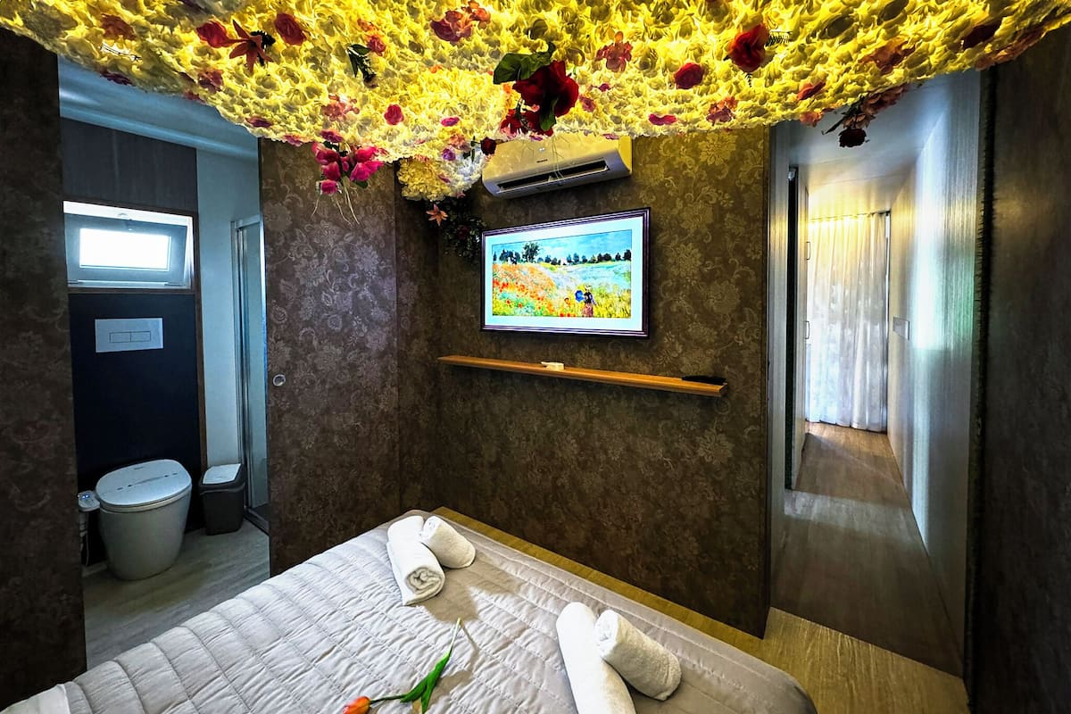 A hotel room with a bed, a TV, a wall-mounted air conditioner, a window, and a bathroom.