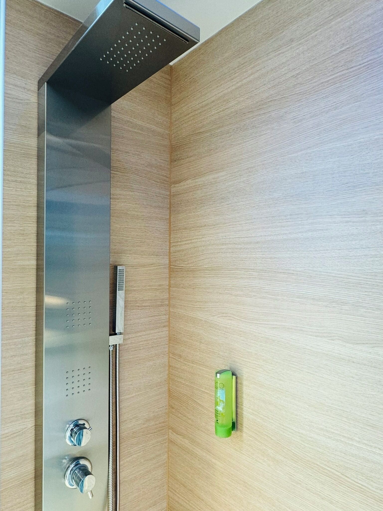 A modern shower enclosure with a control panel and a green bottle on the wall.
