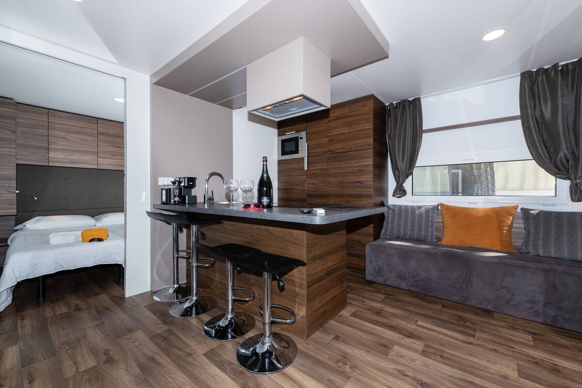 A modern hotel room with a kitchenette, a sofa, a bed, and a bar area.