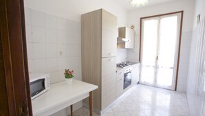A kitchen with white cabinets, a microwave, a sink, and a stove. - Appartamento Lungomare (Campo nell'Elba)