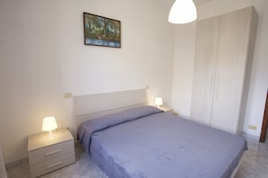 Una camera da letto con un letto, comodini, una lampada, un armadio e un quadro appeso al muro.
