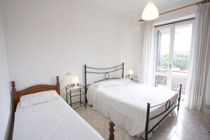 Un dormitorio con dos camas individuales, una mesita de noche con lámpara y una ventana con cortinas.
