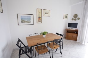 Zona pranzo con tavolo in legno e sedie nere, una pianta in vaso e opere d'arte appese al muro.