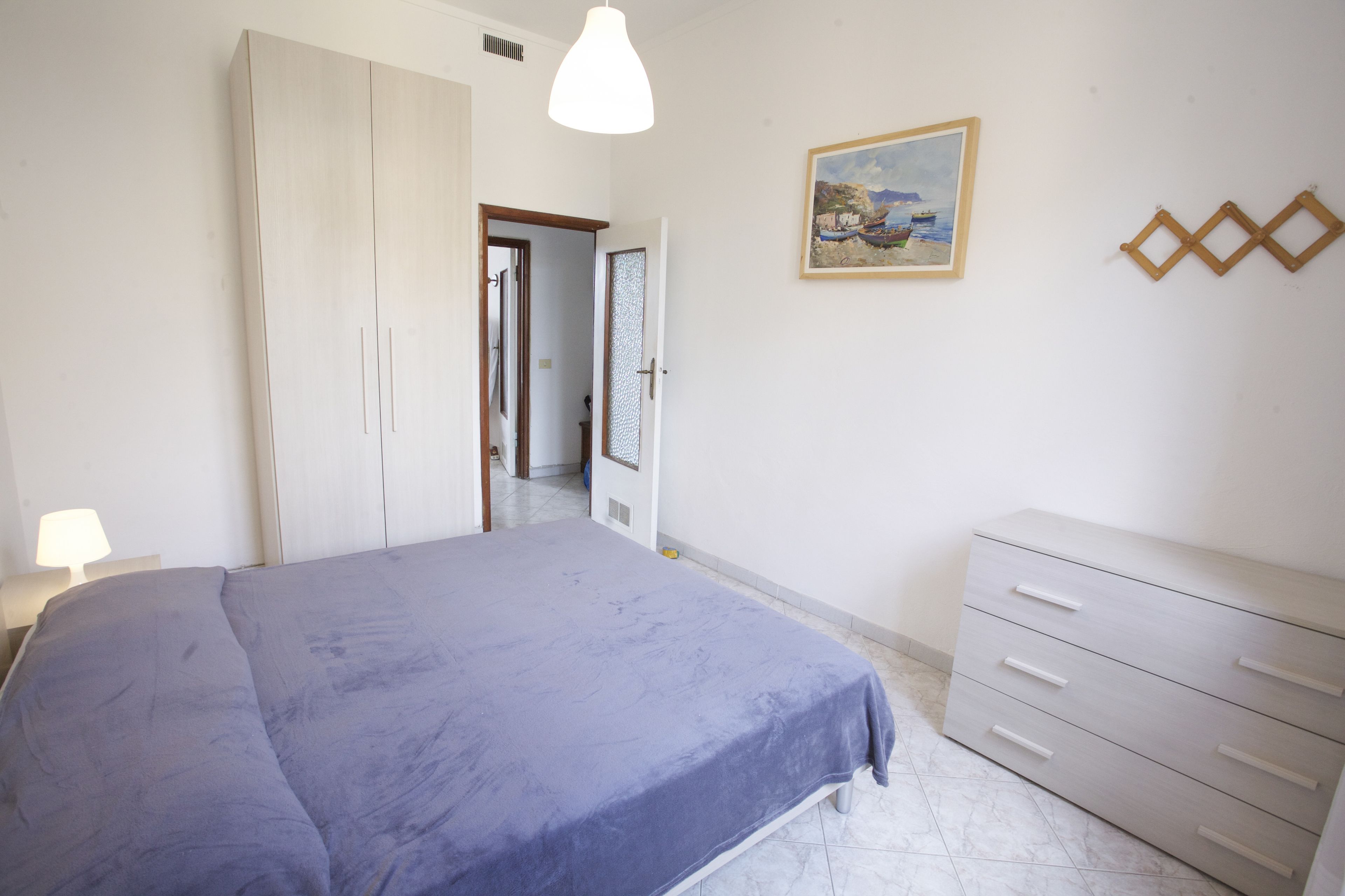 A bedroom with a bed, a dresser, a painting, and a door leading to another room.