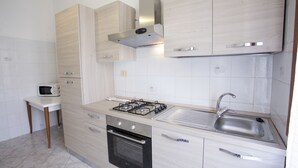 A modern kitchen with a gas stove, oven, stainless steel sink, and light wood cabinetry. - Appartamento Lungomare (Campo nell'Elba)