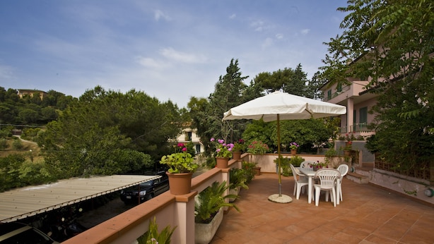 A terrace with a table and chairs, surrounded by potted plants and a white umbrella. - Appartamento Trilo La Padulella (Portoferraio)
