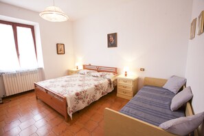 A bedroom with a wooden bed, a smaller bed, a nightstand, a bedside table, a window with a view, and a radiator. - Appartamento Trilo La Padulella (Portoferraio)