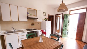 A compact kitchen with white cabinets, a wooden dining table, and green chairs. - Appartamento Trilo La Padulella (Portoferraio)