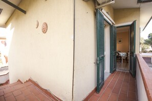 A narrow corridor with a tiled floor, a door with green shutters, and a small table with chairs inside. - Appartamento Trilo Lo Scoglio (Portoferraio)