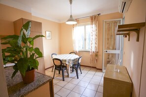 A dining area with a table, chairs, a potted plant, and a window with curtains. - Appartamento Trilo Lo Scoglio (Portoferraio)