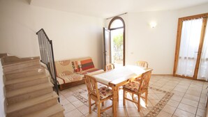 Un comedor con mesa y sillas, una escalera y un sofá con un cojín estampado.
