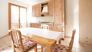 Una cocina con armarios de madera, una mesa de comedor con sillas y un ventanal con cortinas.