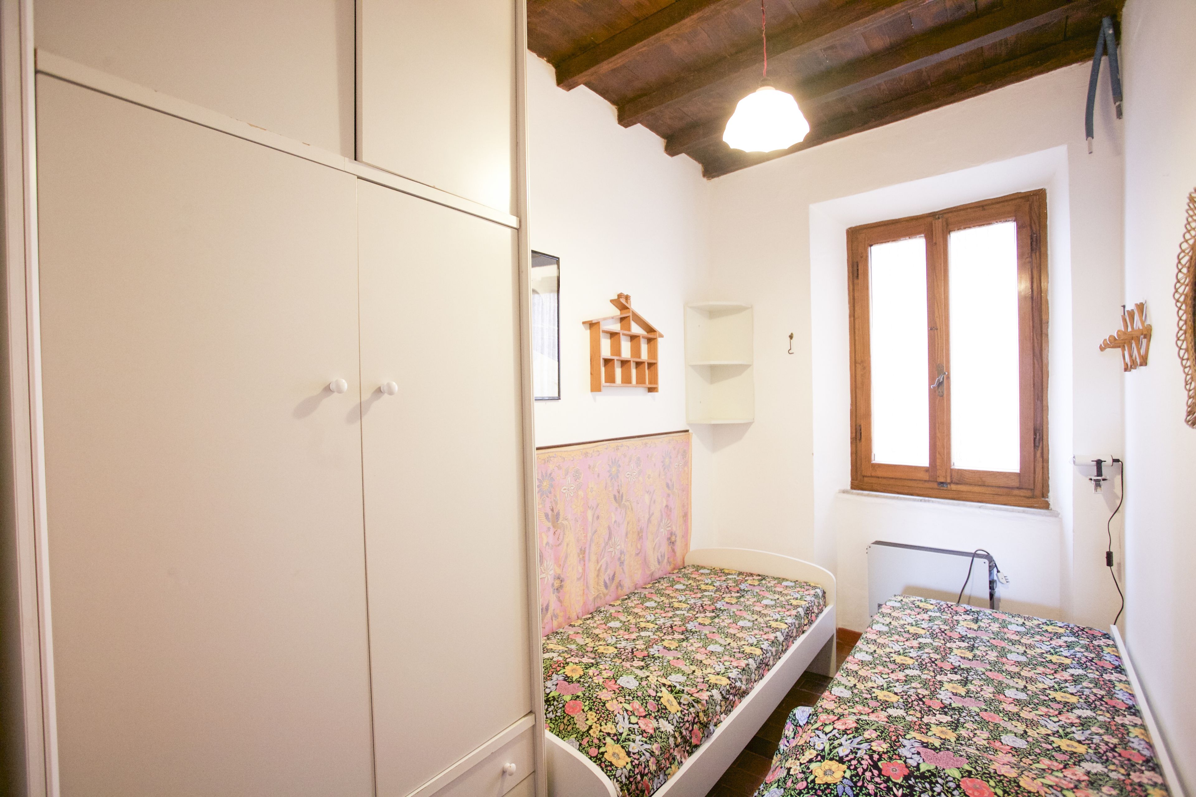 Un dormitorio con dos camas individuales, un armario, una ventana con marcos de madera y una lámpara en el techo.
