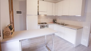 A modern kitchen with white cabinetry, a gas stove, a sink, and a wooden wine rack. - Appartamento il Quadrifoglio (Portoferraio)