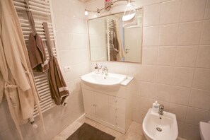 A bathroom with a white sink, a mirror, and a bidet. There are towels hanging on a rack and a brown rug on the floor.