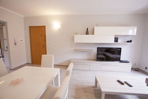 A modern living room with a flat-screen TV, white furniture, and a wooden door.