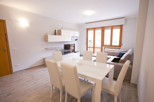 A modern living room with a white sofa, a dining table with chairs, and a TV.
