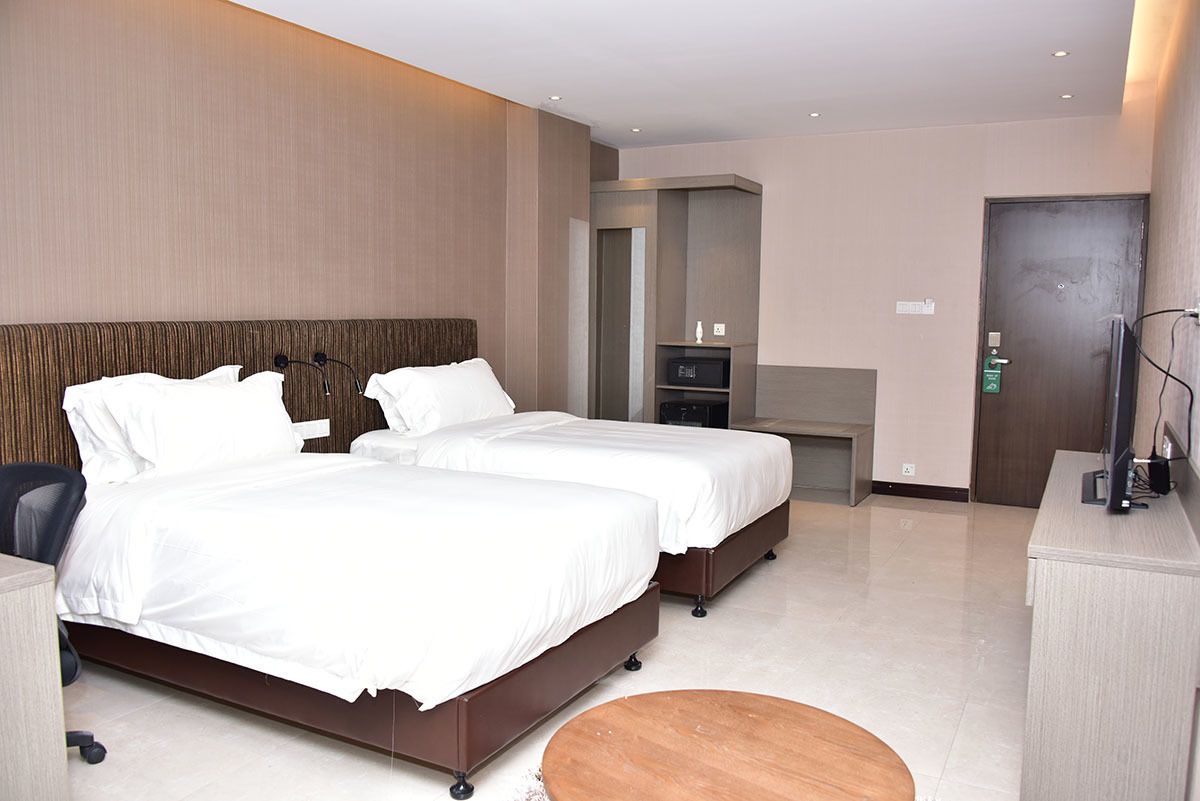 A hotel room with two beds, a desk, a chair, a small round table, and a mirror.