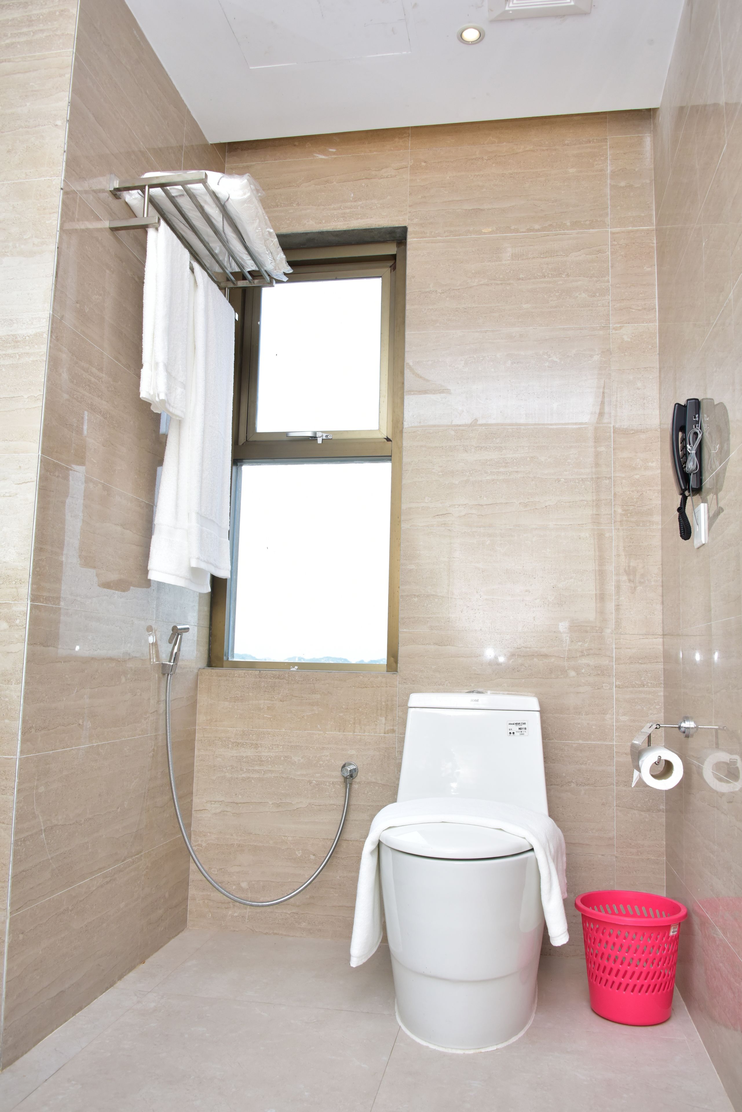 A modern bathroom with a shower, a toilet, a window, and a telephone.
